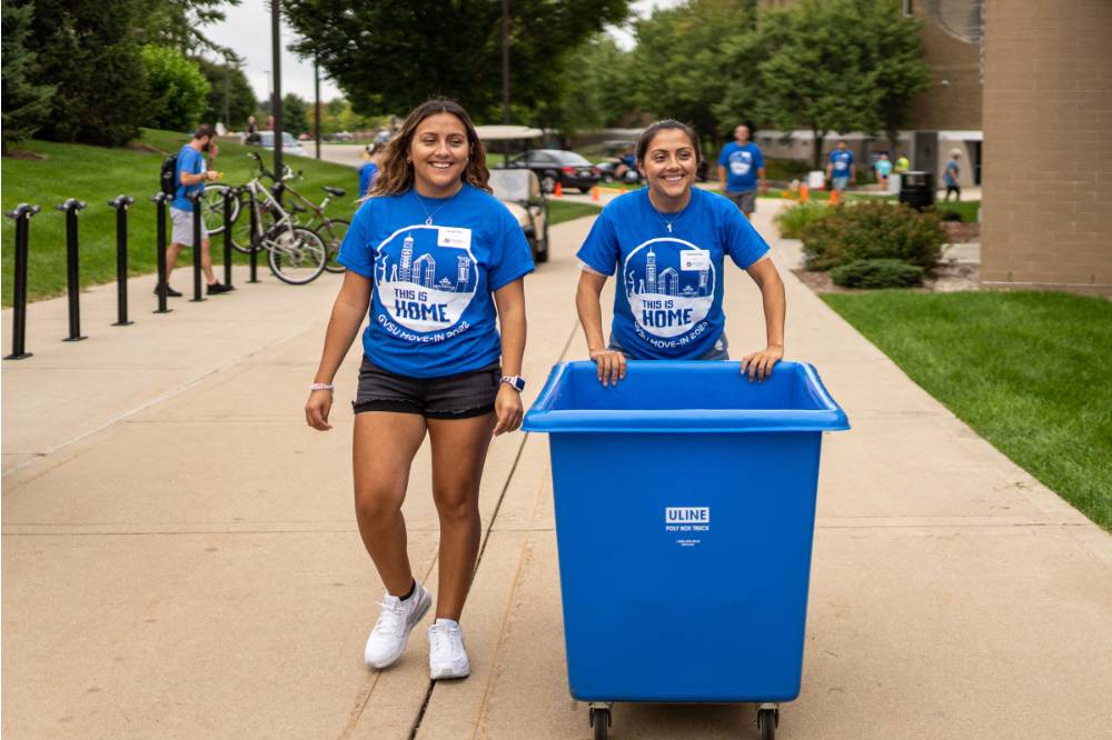 Two alumni with bin to move boxes in